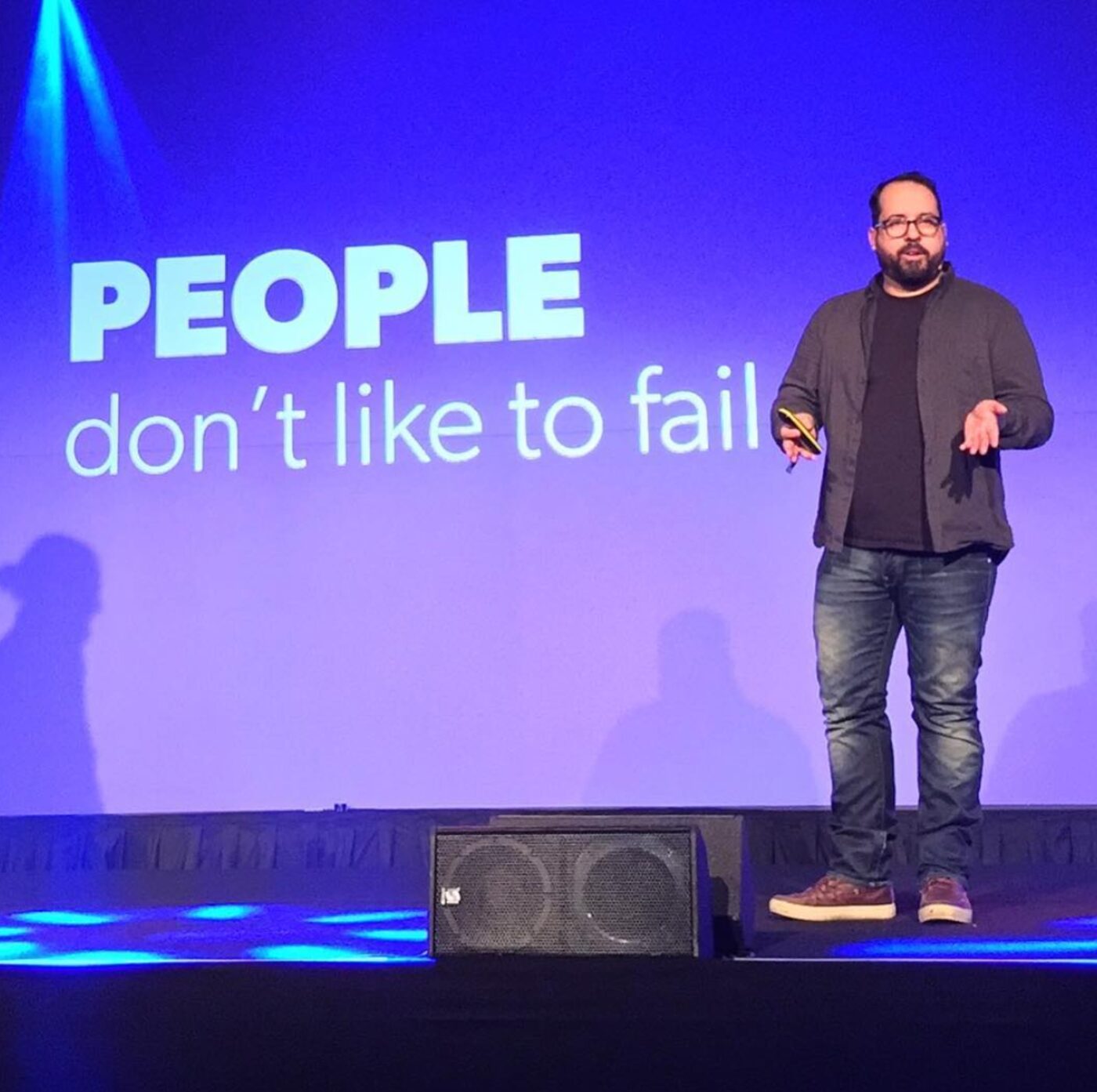 Michel Ferreira on a conference stage, mid-sentence, beside a slide reading &ldquo;People don&rsquo;t like to fail&rdquo;